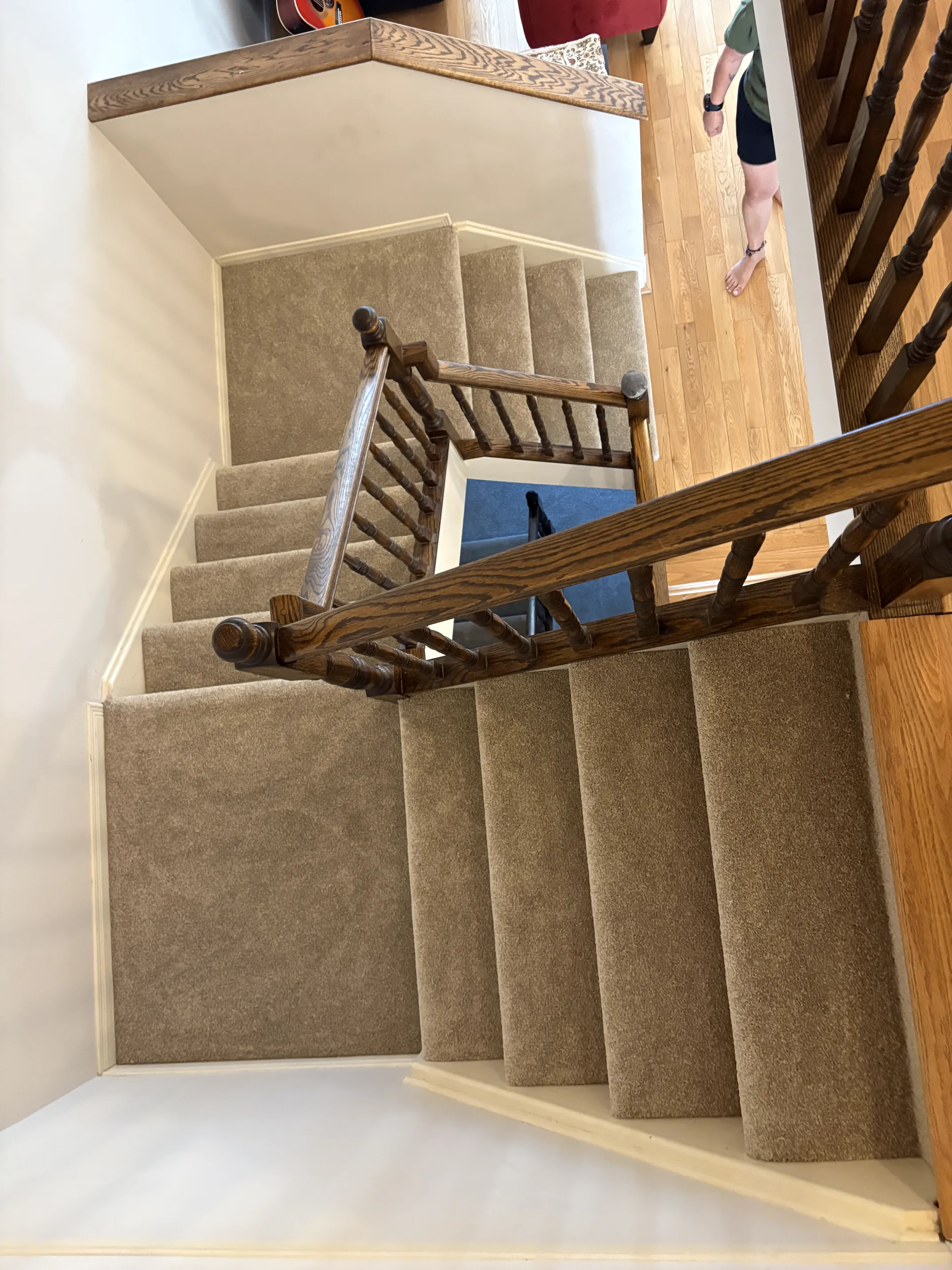 Overhead view down a beige-carpeted staircase and mid-flight landing to the hardwood hall below